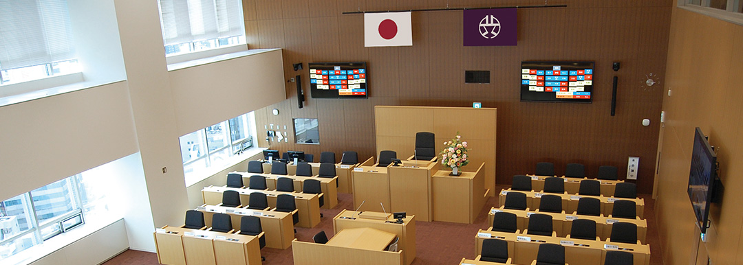 渋谷の街を見渡す景色と吹き抜け天井により開放感が溢れる議場 正面ディスプレイには、投票結果を分かりやすく色分けした採決結果画面を表示中